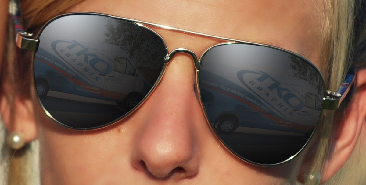 Person wearing aviator sunglasses with TKO Graphix van wrap reflection in the lenses